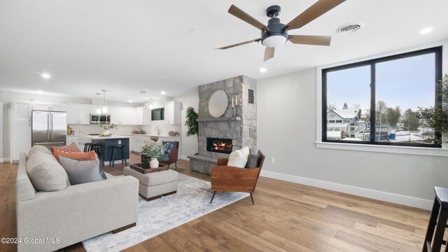 living room featuring ceiling fan, light hardwood / wood-style floors, a stone fireplace, and sink