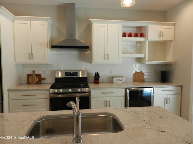 kitchen with light stone countertops, backsplash, gas range, white cabinets, and wall chimney range hood