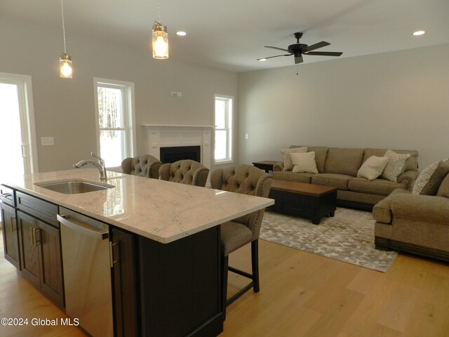 kitchen with decorative light fixtures, sink, light hardwood / wood-style flooring, light stone counters, and dishwasher