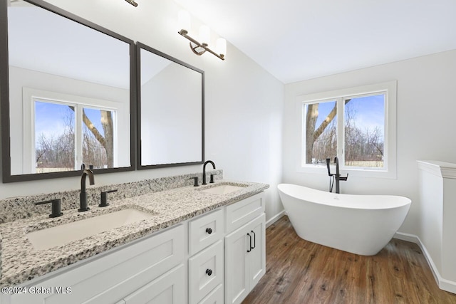 bathroom with wood-type flooring, vanity with extensive cabinet space, double sink, and a bath