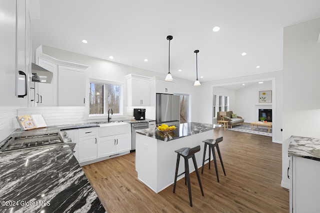 kitchen with sink, light wood-type flooring, white cabinetry, hanging light fixtures, and stainless steel appliances