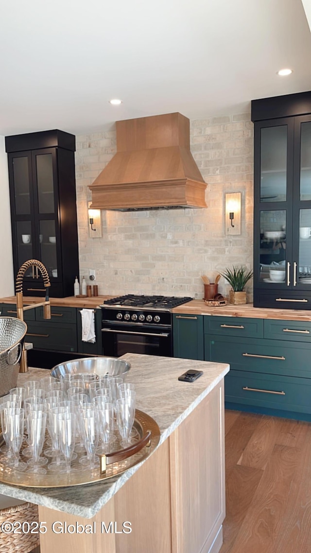 kitchen featuring blue cabinetry, black range with gas cooktop, custom exhaust hood, hardwood / wood-style floors, and backsplash