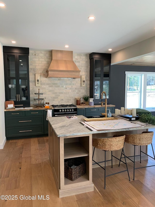 kitchen with premium range hood, high end range, green cabinets, light stone countertops, and light hardwood / wood-style floors