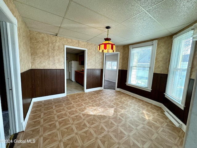 empty room with baseboard heating and a paneled ceiling