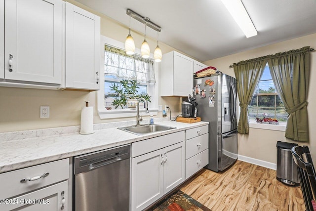 kitchen featuring hanging light fixtures, stainless steel appliances, light hardwood / wood-style floors, sink, and white cabinetry