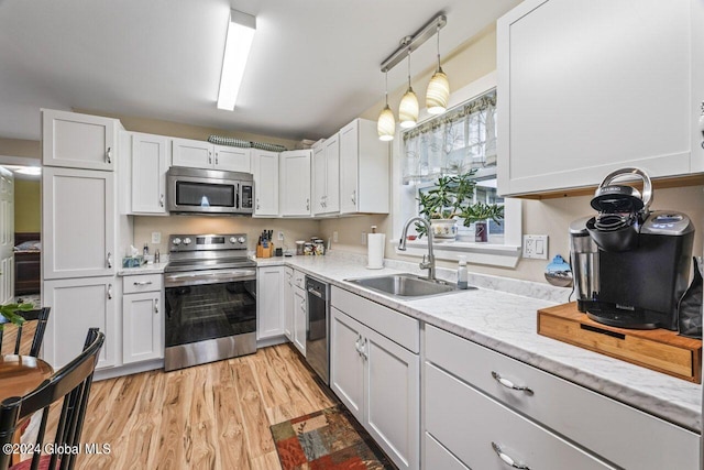 kitchen featuring appliances with stainless steel finishes, light hardwood / wood-style floors, decorative light fixtures, sink, and white cabinets