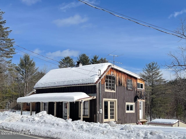 snow covered property with board and batten siding and a chimney