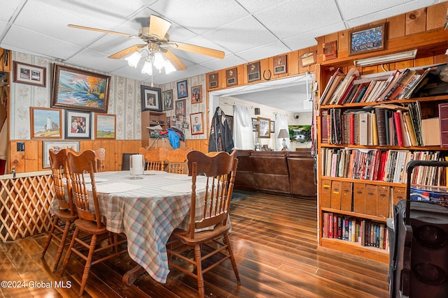 dining room with dark hardwood / wood-style flooring, a paneled ceiling, ceiling fan, and wood walls