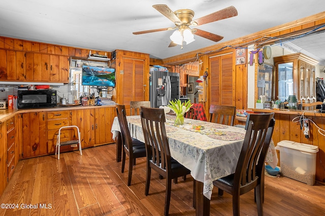 dining room with ceiling fan, wood walls, crown molding, and light hardwood / wood-style flooring