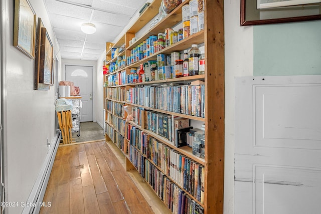 hall with light wood-type flooring, a drop ceiling, and a baseboard heating unit