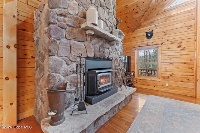 unfurnished living room with high vaulted ceiling, wooden ceiling, light hardwood / wood-style floors, a wood stove, and wood walls