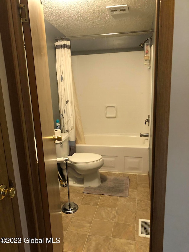 bathroom with toilet, tile flooring, shower / bath combo with shower curtain, and a textured ceiling