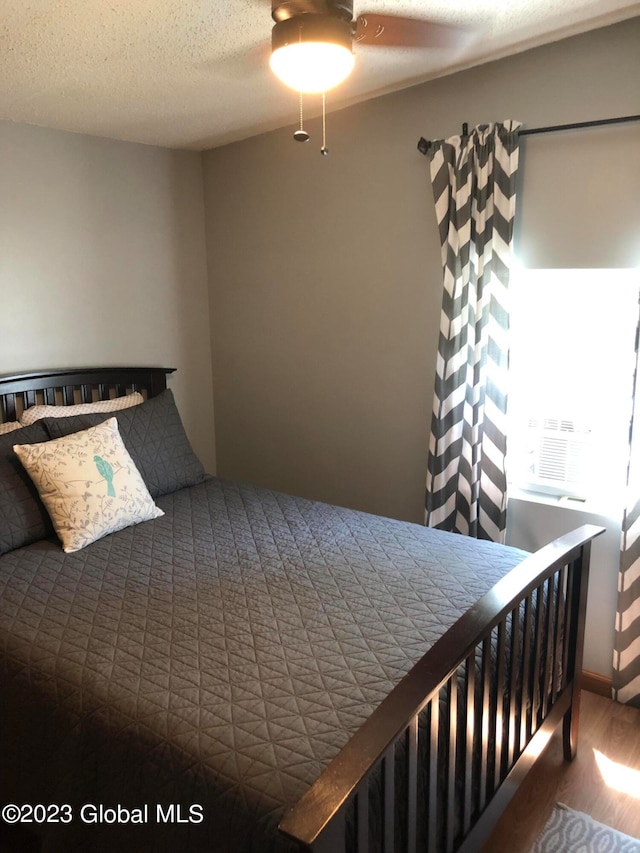 bedroom with hardwood / wood-style floors, ceiling fan, and a textured ceiling