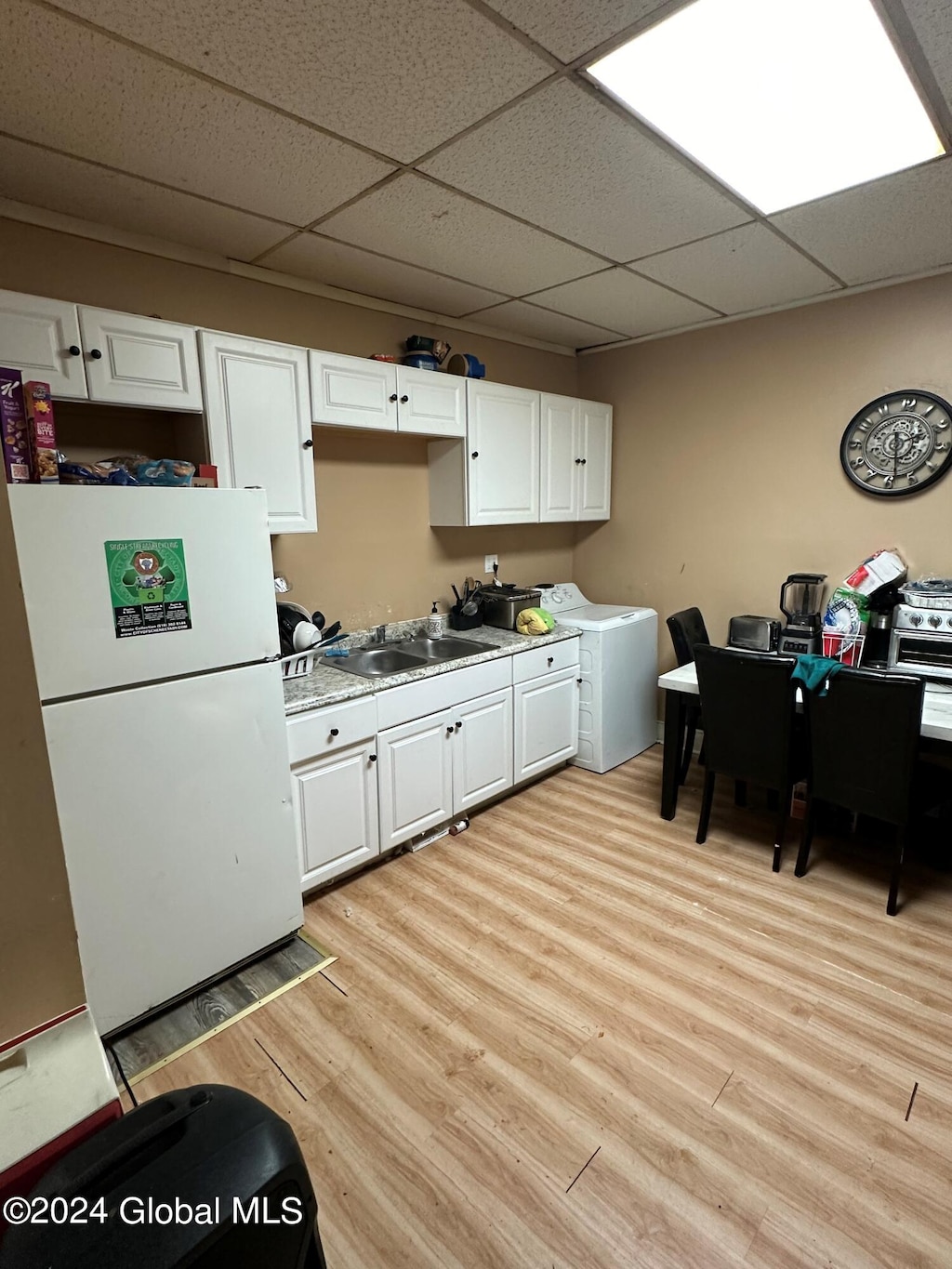 kitchen with white refrigerator, light wood-type flooring, washer / dryer, sink, and white cabinets