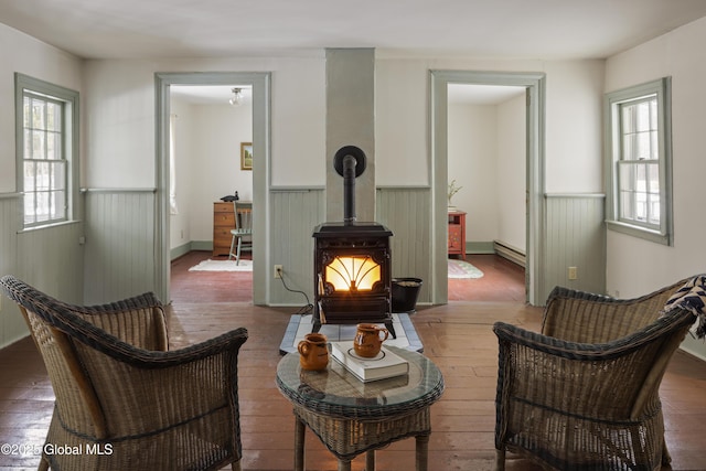 living area with a baseboard heating unit, dark hardwood / wood-style floors, a wealth of natural light, and a wood stove