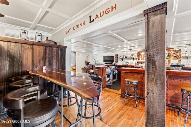 dining space with coffered ceiling, light hardwood / wood-style flooring, and bar