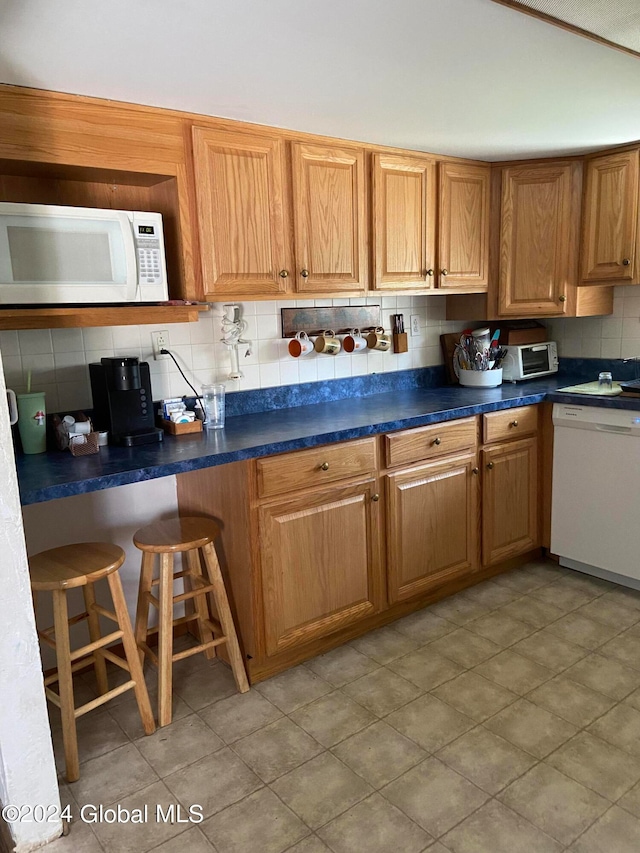 kitchen featuring white appliances, tasteful backsplash, light tile floors, and a kitchen bar