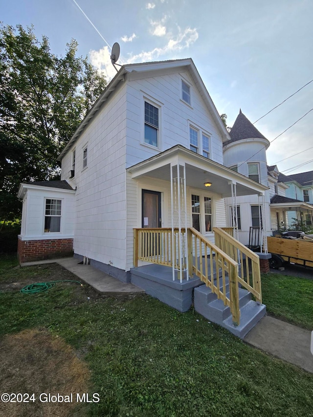 back of property featuring covered porch, brick siding, and a lawn