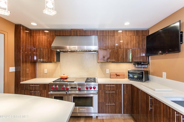 kitchen with range with two ovens, light hardwood / wood-style flooring, wall chimney range hood, and backsplash