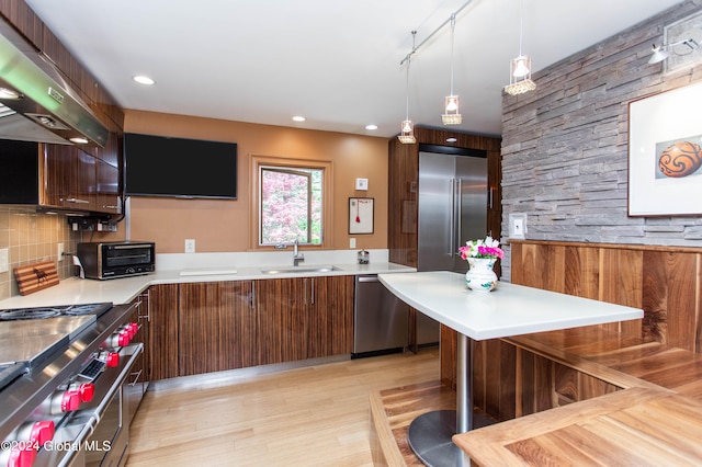 kitchen with sink, wall chimney range hood, light wood-type flooring, decorative light fixtures, and stainless steel appliances