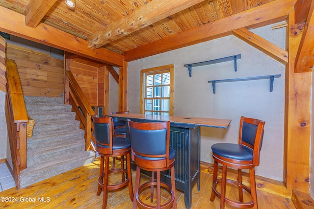 bar with beamed ceiling, wooden ceiling, and light hardwood / wood-style flooring