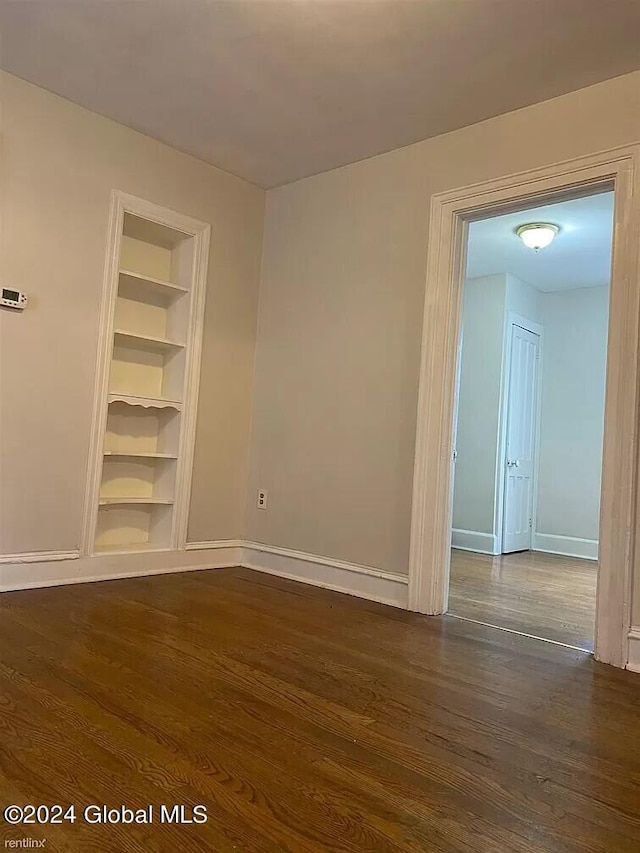 unfurnished room featuring dark wood-type flooring and built in shelves