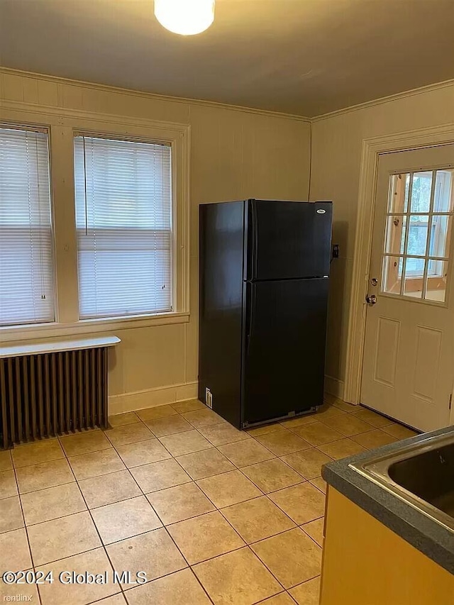 kitchen featuring black refrigerator, light tile flooring, and radiator