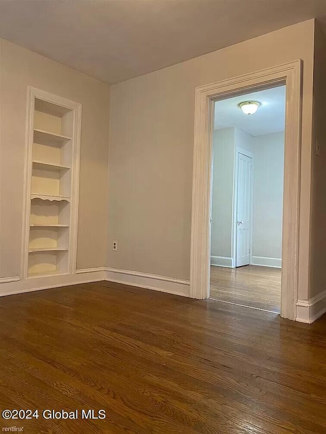 empty room featuring built in shelves and dark wood-type flooring