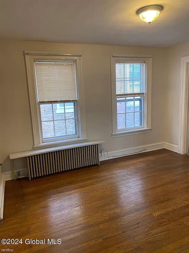 spare room with radiator heating unit and dark wood-type flooring