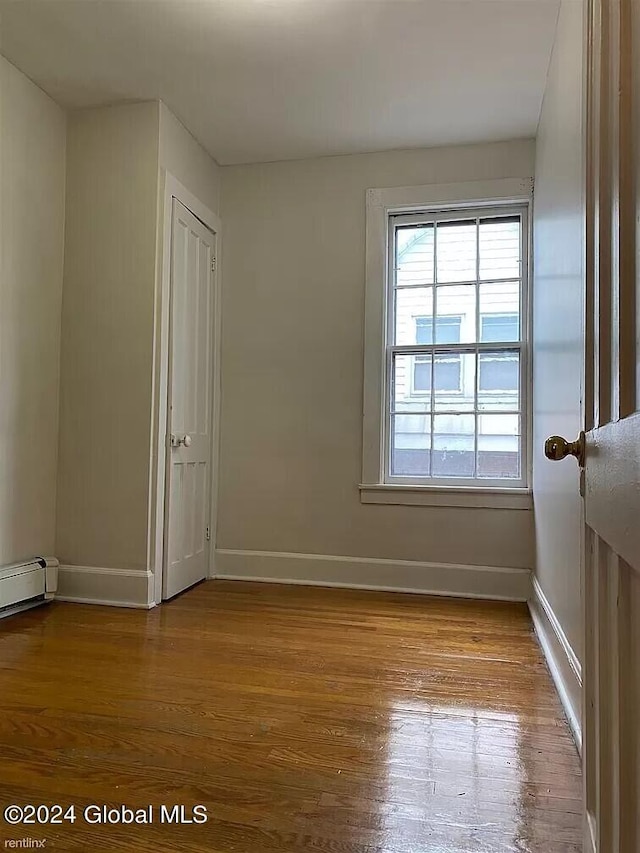 unfurnished room featuring a baseboard heating unit and wood-type flooring