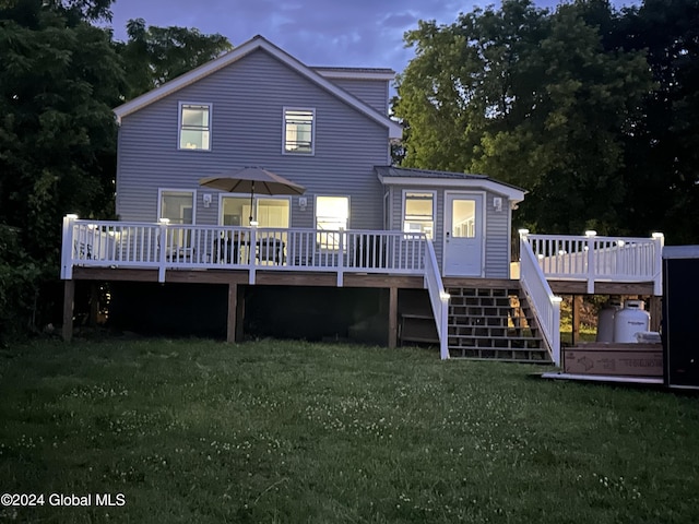 back house at dusk featuring a lawn and a deck