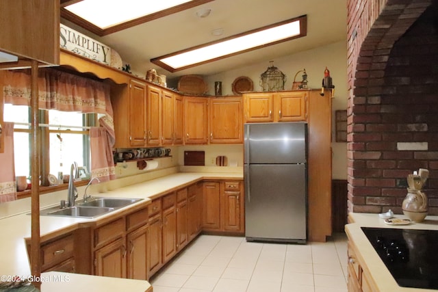 kitchen with black electric stovetop, stainless steel fridge, light tile flooring, sink, and lofted ceiling