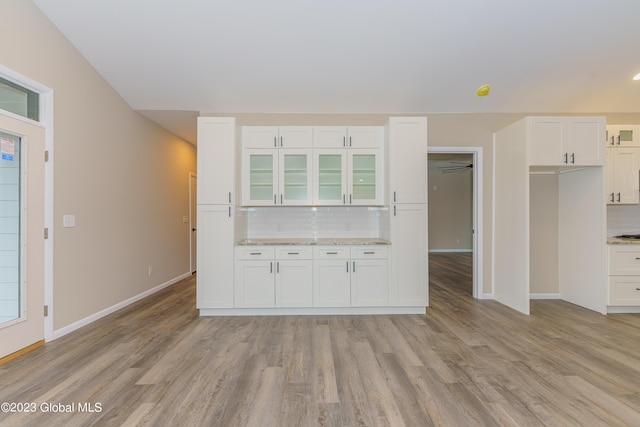 kitchen with white cabinets, light wood-type flooring, tasteful backsplash, and light stone countertops