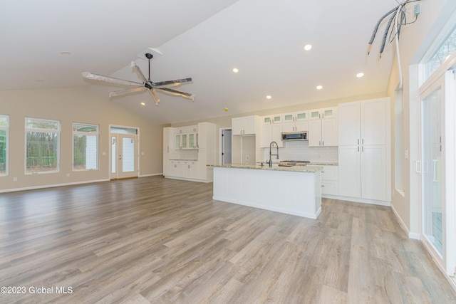 kitchen with a kitchen island with sink, white cabinets, vaulted ceiling, decorative backsplash, and light wood-type flooring