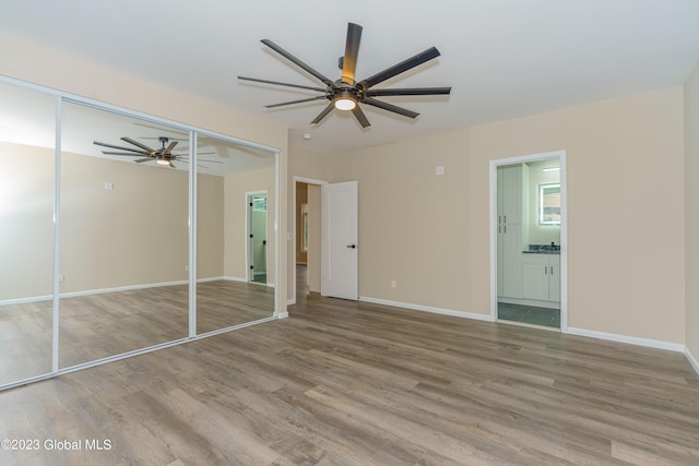 unfurnished bedroom featuring ensuite bath, ceiling fan, a closet, and hardwood / wood-style flooring