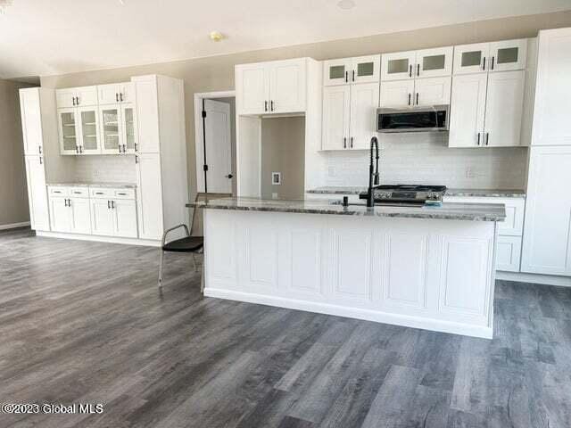 kitchen featuring tasteful backsplash, dark hardwood / wood-style flooring, dark stone countertops, an island with sink, and white cabinets