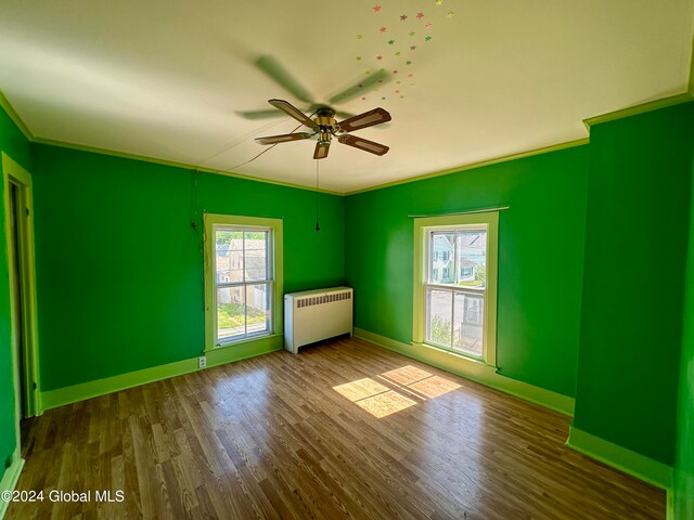 empty room with crown molding, ceiling fan, wood-type flooring, and radiator