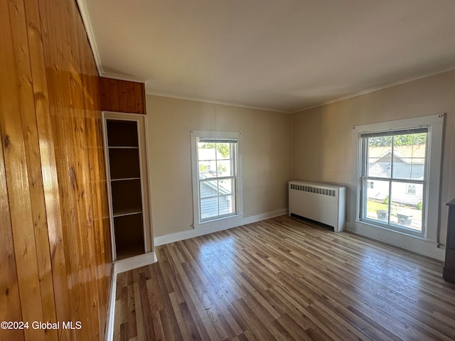 empty room featuring crown molding, wooden walls, hardwood / wood-style floors, and radiator