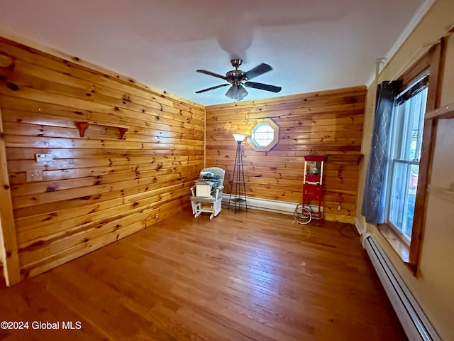 unfurnished room with wooden walls, ceiling fan, a baseboard radiator, and wood-type flooring