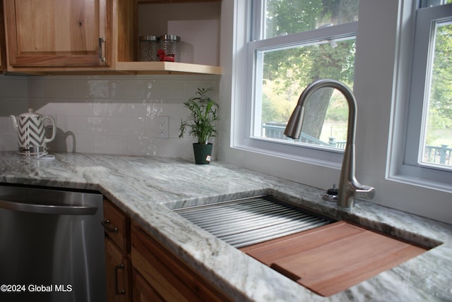 kitchen featuring tasteful backsplash, dishwasher, sink, and light stone countertops