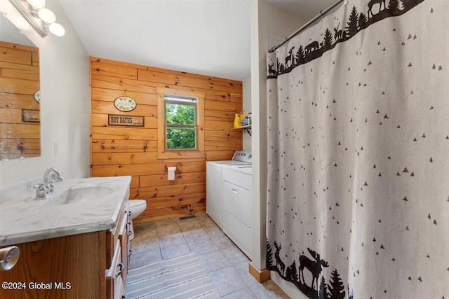 bathroom featuring tile floors, wooden walls, independent washer and dryer, vanity with extensive cabinet space, and toilet