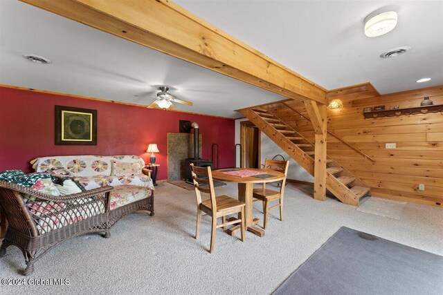 carpeted living room featuring wood walls, beam ceiling, and ceiling fan