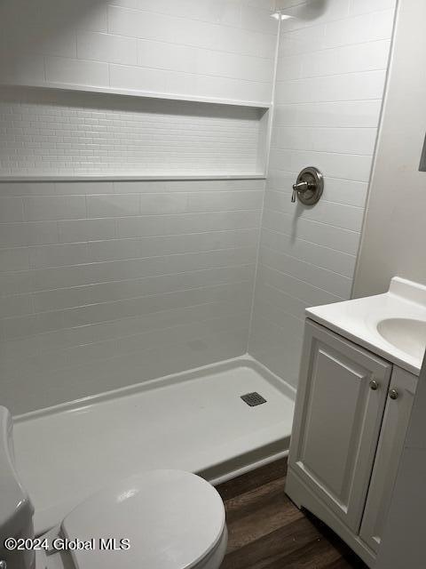 bathroom with toilet, vanity, hardwood / wood-style floors, and tiled shower