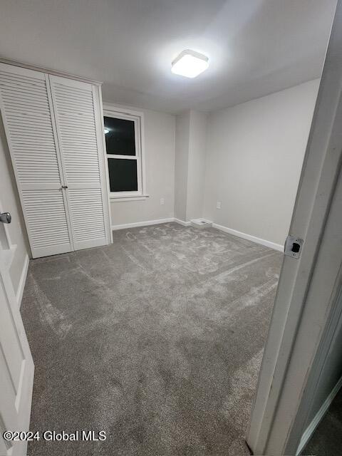 unfurnished bedroom with dark carpet and a closet