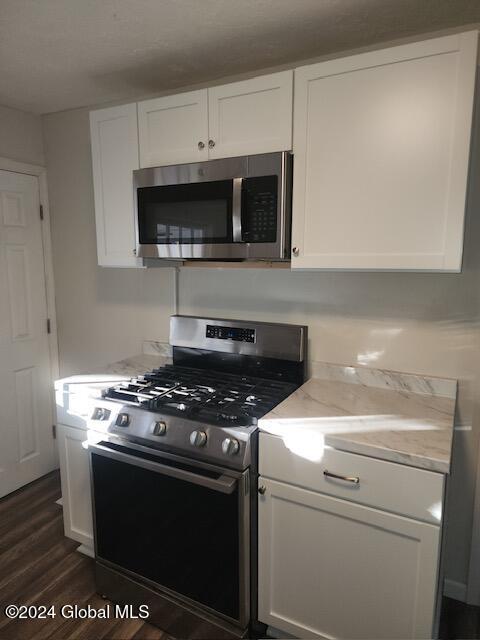 kitchen featuring light stone counters, dark hardwood / wood-style flooring, white cabinets, and stainless steel appliances