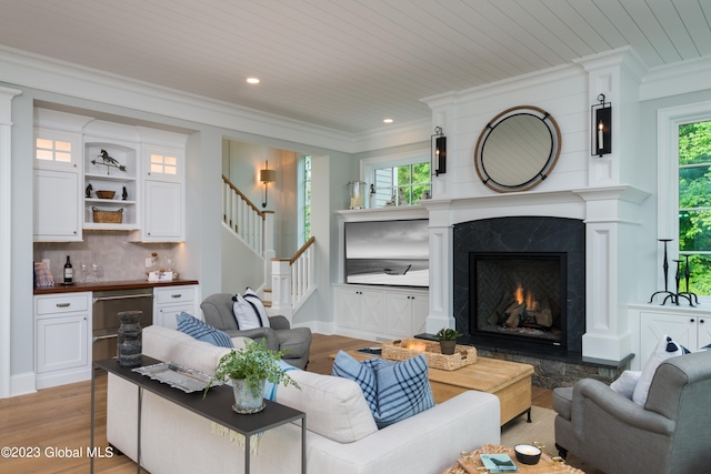 living room with a premium fireplace, ornamental molding, wooden ceiling, and light wood-type flooring