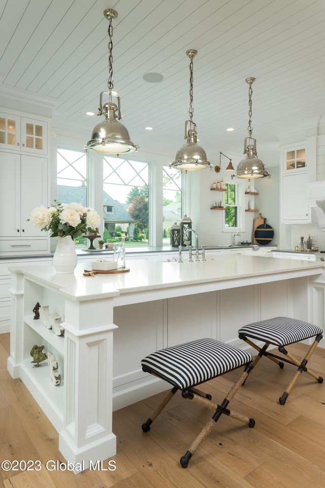 kitchen with light hardwood / wood-style floors, white cabinets, decorative light fixtures, and a center island with sink