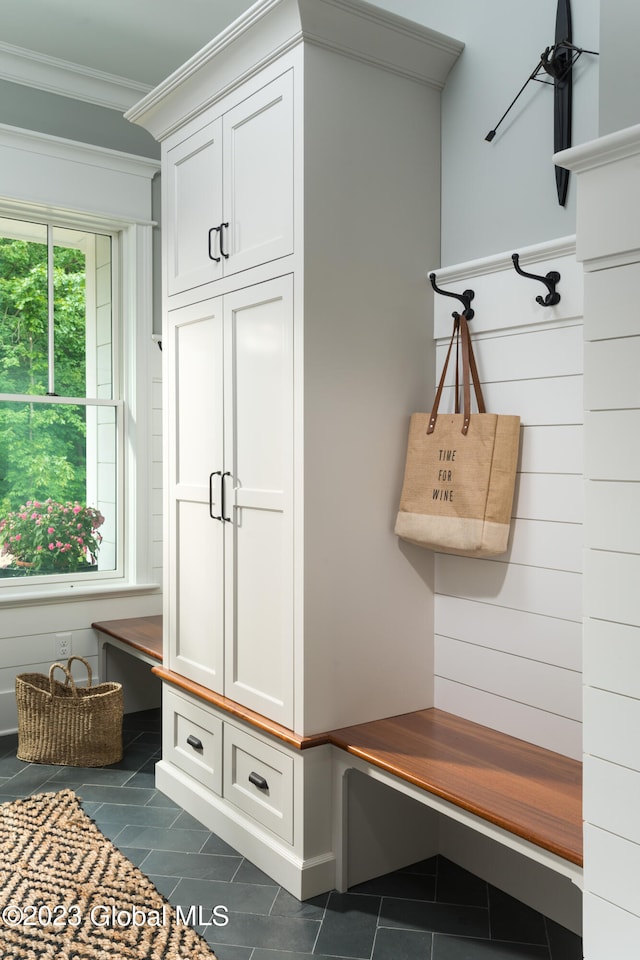 mudroom with ornamental molding, wooden walls, and dark tile patterned flooring