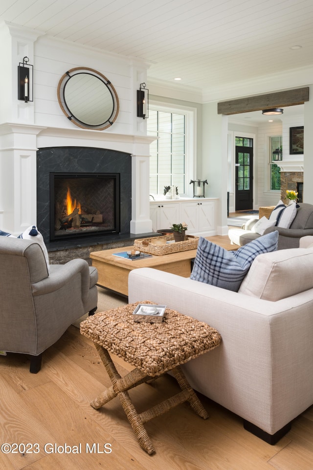 living room featuring a premium fireplace, light hardwood / wood-style flooring, ornamental molding, and wooden ceiling