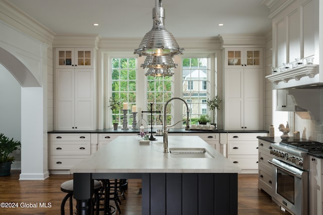 kitchen featuring high end stove, an island with sink, pendant lighting, white cabinets, and dark hardwood / wood-style flooring